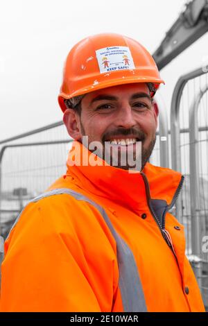 Safety marshall trägt orange hohe viz Jacke und Sicherheitshelm mit sozialen Distanzierung in Betrieb 2m auseinander Halten Sie sicher in Bournemouth, Dorset UK Stockfoto