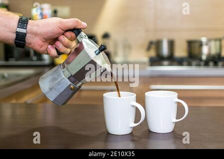 Kaffee in der Brüheinheit zubereiten. Zwei weiße Tassen und giessen heißen, dampfenden Kaffee. Stockfoto