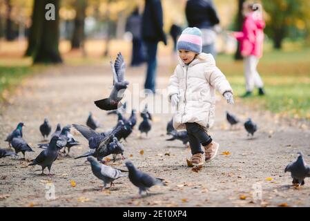 Junge blonde Mädchen jagen Vögel im Park, Herbst Stockfoto