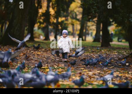 Junge blonde Mädchen jagen Vögel im Park, Herbst Stockfoto