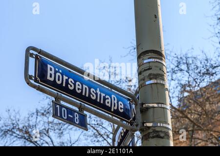 Blaue Straßenschild Börse auf einem grauen Laternenpfosten mit Befestigungen. Haus Nummer acht bis zehn auf dem Schild. Haus mit Fensterfassade und Bäumen im Frühjahr in Th Stockfoto