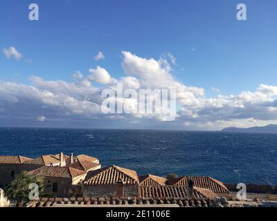 Aspekt der Ziegeldächer in der alten Zitadellenstadt Monemvassia, Griechenland, mit dem blauen Meer und Wolkenlandschaft im Hintergrund Stockfoto