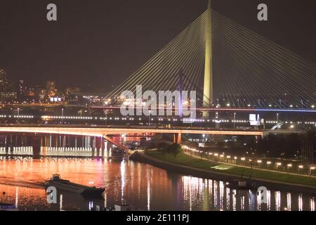 Sava Fluss in Belgrad, mit neuer und alter Brücke und Bootstour. Brücke von Neonlicht beleuchtet Stockfoto