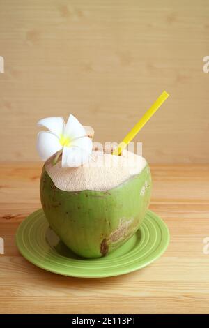Vertikales Bild von frischem jungen Kokosnusssaft mit einem blühenden Frangipani Blume auf Holz Hintergrund Stockfoto