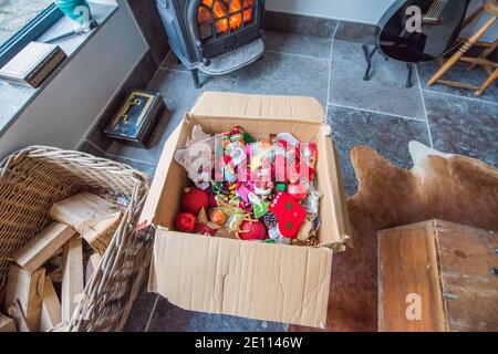 Braune Pappschachtel mit einem Durcheinander von Familie bunte Weihnachten Baumschmuck vor einem Holzbrenner auf einem Stein Boden wird weggepackt Stockfoto