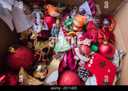 Braune Pappschachtel mit einem Durcheinander von Familie bunte Weihnachten Baumschmuck vor einem Holzbrenner auf einem Stein Boden wird weggepackt Stockfoto