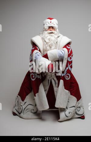 Cool grau behaart mit langem Bart Weihnachtsmann in rot Kleidung posiert auf grauem Studio Hintergrund Stockfoto
