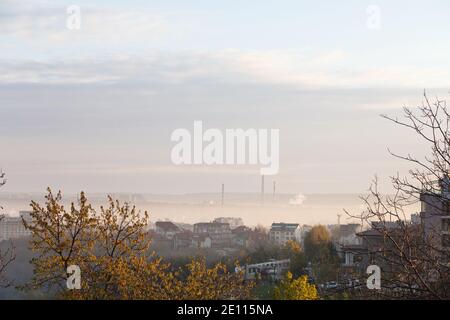 Herbstlandschaft. Nebel bedeckt das Stadtzentrum. Bäume im Vordergrund und blauer Himmel im Hintergrund. Stockfoto