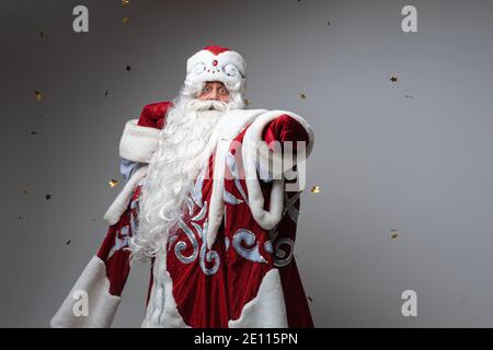 Lustige ältere männliche Santa Claus Point von Hand in rot Fäustling auf grauem Hintergrund mit Kopierplatz Stockfoto