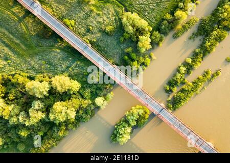 Luftaufnahme einer schmalen Straßenbrücke, die sich über einen schlammigen, breiten Fluss in grüner ländlicher Umgebung erstreckt. Stockfoto