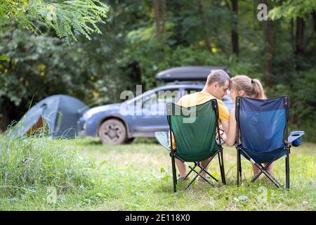 Ein glückliches Paar sitzt auf Stühlen auf dem Campingplatz und umarmt sich. Reise-, Camping- und Urlaubskonzept. Stockfoto