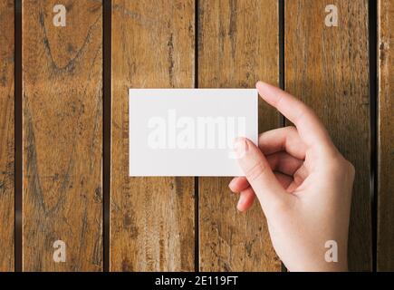 Frau Hand halten leere weiße Visitenkarte Mockup auf einem Holztisch. Logo und Branding Design Vorlage Konzept Stockfoto