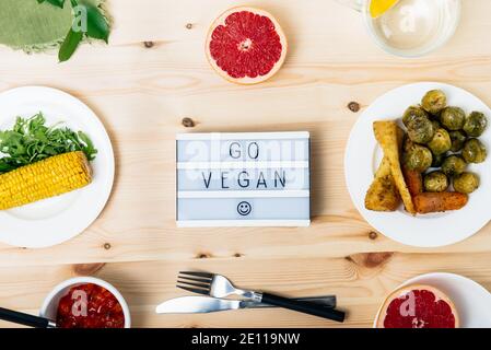 Draufsicht pflanzliche Gerichte mit Go vegan Botschaft auf Leuchtbrett. Mahlzeit Portion von gebackenem Gemüse wie rosenkohl, Petersilienwurzel, Karotten, Mais Stockfoto