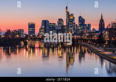 Frankfurter Skyline am Abend bei Sonnenuntergang. Hochhäuser aus dem Finanzviertel und dem Main mit Reflexionen. Beleuchtete Häuser Stockfoto