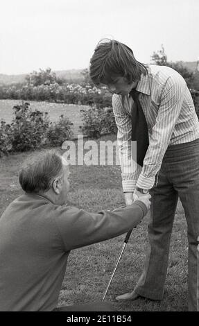 70er Jahre, historisch, draußen auf einem Grasrand von einem Putting Green, ein älterer männlicher Golfprofi zeigt einen jungen Amateur männlichen Golfspieler, der den Golfclub hält, der "Vardon Grip", auch bekannt als der überlappende Griff, benannt nach dem langen Golfer Harry Vardon, einem sechsfachen Open Champion. Um das Golfspiel gut zu spielen, ist der richtige Griff wichtig. Beachten Sie die Kleidung des langhaarigen jungen Mannes, der ein Hemd und eine kipper Krawatte und Flair Hose der Zeit trägt. Stockfoto