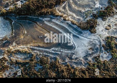 Abstrakter Hintergrund, Eis auf gefrorener Pfütze geknackt. Eisfragmente auf gefrorenem Wasser. Das Eis zerbrochene Stücke.Eis auf einem gefrorenen Wasser Pfütze auf dem Schlamm hinein Stockfoto