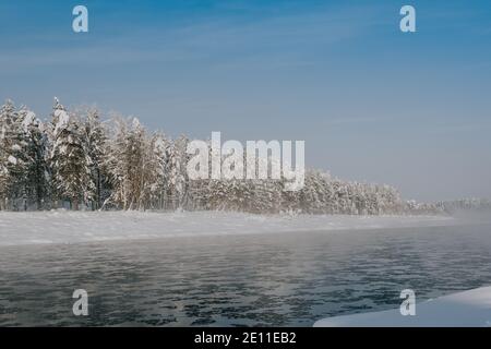 Frostiger Nebel über dem Winterfluss mit Schnee und Wald am Ufer. Erstes Eis am See an kalten Tagen. Stockfoto