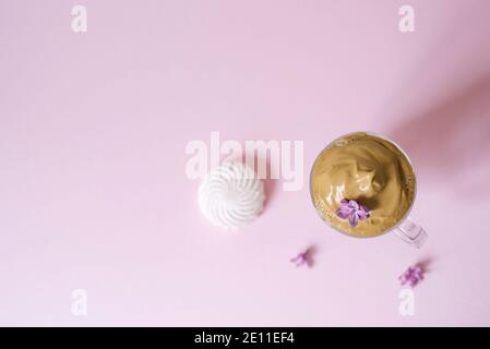 Schöner Dalgon Kaffee trinken. Kaffeebecher mit Schaum und Fliederblüte auf einem lila rosa Hintergrund. Draufsicht Stockfoto