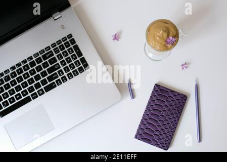 Dalgona Kaffee in einer klaren Tasse, Notizblock, Stift und Computer auf dem Tisch. Draufsicht. Kaffeepause am Arbeitsplatz. Stockfoto