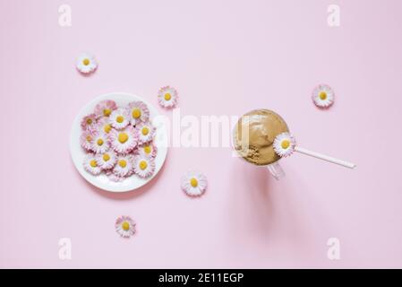 Dalgona Kaffee in einer transparenten Tasse mit einem Papierrohr, ein Teller mit Blumen Gänseblümchen. Draufsicht Stockfoto