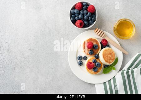 Hüttenkäse fritters mit Sommerbeeren und Honig. Draufsicht, grauer Betonhintergrund mit Kopierraum Stockfoto