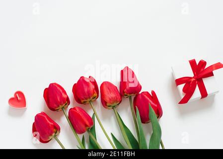 Valentinstag Romantische Hintergrund. Rote Tulpen, ein Geschenk mit Schleife und Kerzenherzen auf weißem Hintergrund mit Kopierraum. Flach liegend Stockfoto