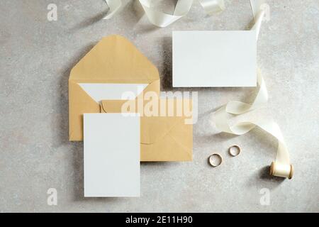 Leere Hochzeitseinladungskarten Mockups, Umschläge, Band und Ringe auf Betontisch. Flach liegend, Draufsicht. Stockfoto