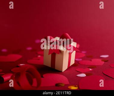 Frohes st. Valentinstagskonzept mit Bastelpapier-Geschenkbox, roten Papierherzen, Bögen vor dunkelrotem Hintergrund mit Platz für Text. Stockfoto