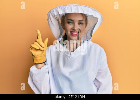 Schöne blonde kaukasische Frau trägt schützende Imker Uniform zeigen und Zeigt mit dem Finger Nummer eins und lächelt zuversichtlich und Glücklich Stockfoto