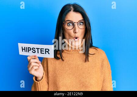 Mittlere Alter Brünette Frau hält Papier mit Hipster Wort erschrocken und erstaunt mit offenem Mund für Überraschung, Unglauben Gesicht Stockfoto