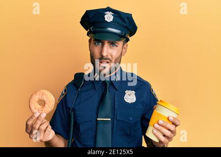 Handsome hispanic Polizei Mann essen Donut und trinken Kaffee ahnungslos und verwirrt Ausdruck. Zweifel Konzept. Stockfoto