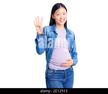 Junge schöne chinesische Frau schwanger erwartet Baby zeigen und zeigen mit den Fingern Nummer vier beim Lächeln zuversichtlich und glücklich. Stockfoto