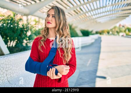 Junge blonde Mädchen mit ernsten Ausdruck verletzt mit Arm Sling stehen im Park. Stockfoto