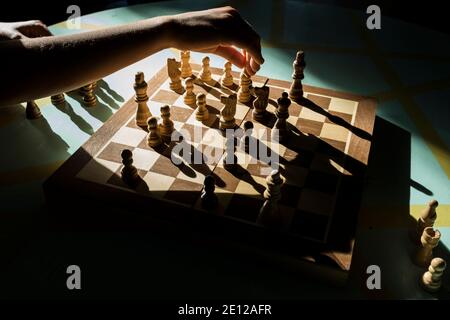 Eine Nahaufnahme der Hand eines jungen Mädchens, die Schachfiguren in dramatischem natürlichem Licht bewegt. Stockfoto