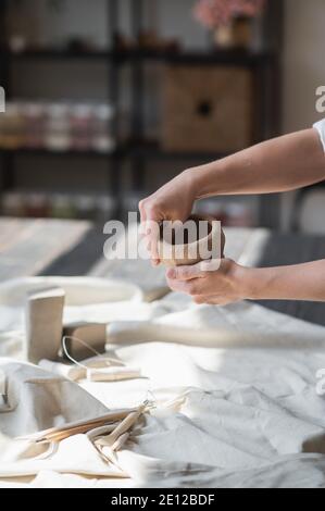 Eine junge Töpferin, die Topf in ihrem eigenen Arbeitsplatz macht. In einem geräumigen Studio stehend und mit ihren Händen die Form des zukünftigen Produkts erschaffen. Stockfoto