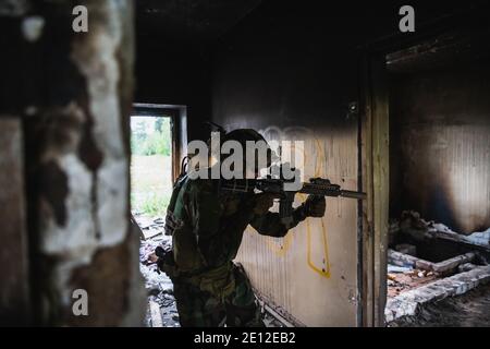 Soldat in voller US MARSOC bewaffnet mit Sturmgewehr durch das verlassene Gebäude laufen. Militärischer Zusammenstoß. Stockfoto