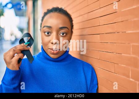 Junge afroamerikanische Frau mit ernsthaftem Ausdruck hält schwarzes Awareness Band an der Stadt. Stockfoto