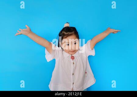 Ein süßes junges asiatisches Mädchen fühlt sich sorglos mit weit geöffneten Armen. Einfacher hellblauer Hintergrund. Stockfoto