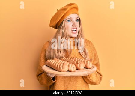 Schöne junge kaukasische Mädchen tragen französisch Look mit Baskenmütze hält Baguettes Brot wütend und verrückt schreien frustriert und wütend, schreien mit einem Stockfoto