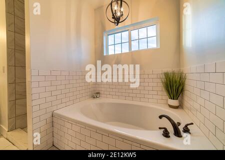 Eingebaute ovale Badewanne mit schwarzem Wasserhahn gegen weiße Fliesen Wand des Badezimmers Stockfoto