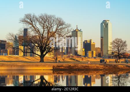 Menschen entspannen im Trammel Crow Park mit Blick auf die Skyline von Dallas, Texas im Hintergrund und reflektierenden Teich im Vordergrund. Stockfoto