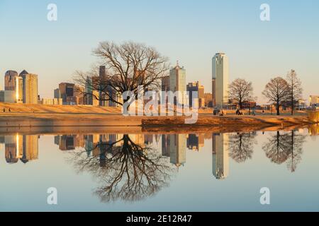 Menschen entspannen im Trammel Crow Park mit Blick auf die Skyline von Dallas, Texas im Hintergrund und reflektierenden Teich im Vordergrund. Stockfoto