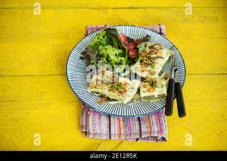 Schwäbische Ravioli mit gerösteten Zwiebeln und runny Käse, serviert mit Salat auf EINEM Gelben Holztisch Stockfoto