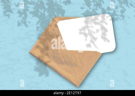Ein Umschlag mit einem Blatt weißem Strukturpapier auf dem blauen Hintergrund der Wand. Mockup Overlay mit den Pflanzenschatten. Natürliche Lichtstrahlen Stockfoto