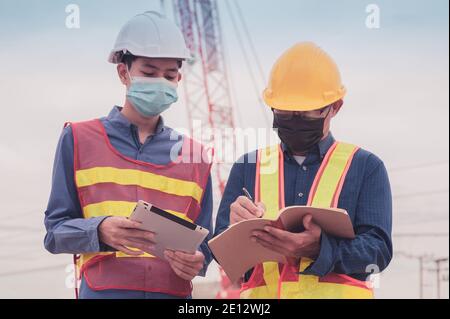Zwei Engineer Wear Gesichtsmaske schreiben auf Buch Arbeiten auf der Baustelle Bau, Engineer Protect coronavirus covid 19 von Gesichtsmaske Stockfoto