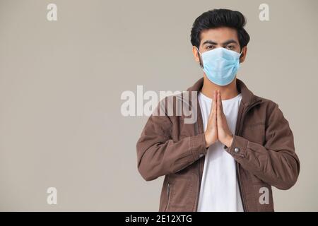 EIN JUNGER MANN TRÄGT MASKE GRUSS MIT GEFALTETEN HÄNDEN Stockfoto