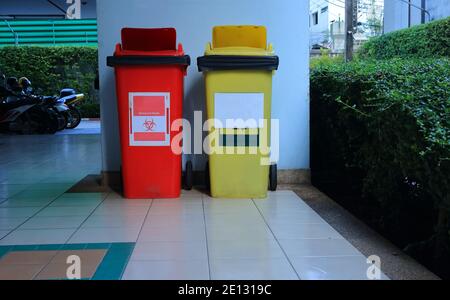Nahaufnahme roter Abfalleimer, der auf dem gefliesten Boden daneben steht Gelber Recyclingbehälter an der blauen Wand in einem Gebäude Stockfoto