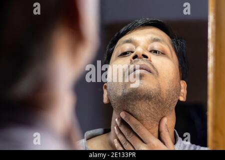 Ein indischer Mann mittleren Alters, der seinen eigenen unrasierten Blick ansieht Bart im Spiegel Stockfoto