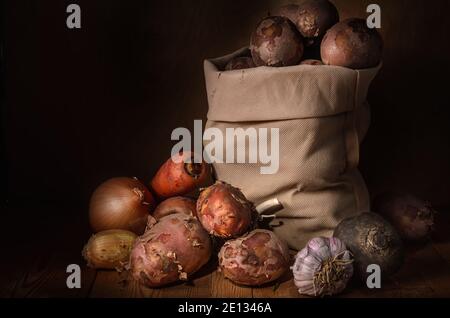 Kartoffeln in einem Stoffbeutel und anderes Gemüse in einem Rustikaler Stil auf einem dunklen Holzhintergrund Stockfoto