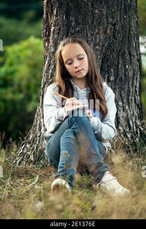 Teengirl schreibt Molkerei in einem Notizbuch, während er im Park sitzt. Stockfoto